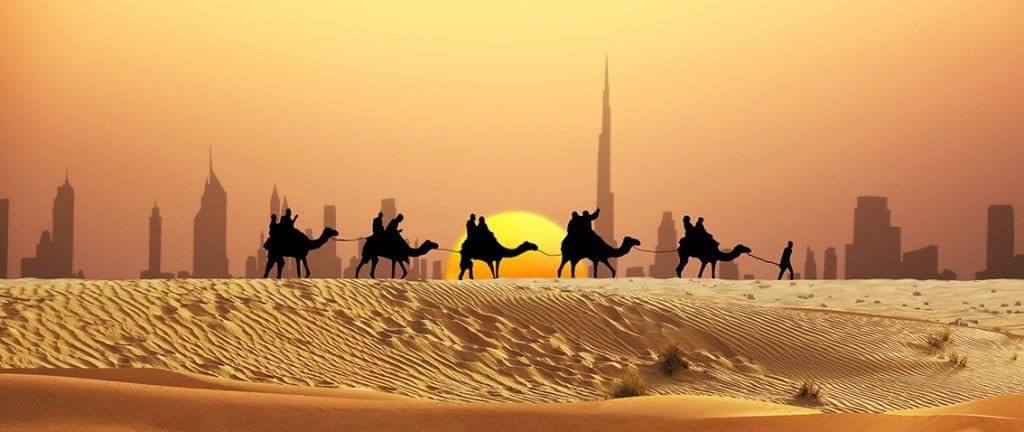 Desert safari caravan in front of Dubai skyline during sunset