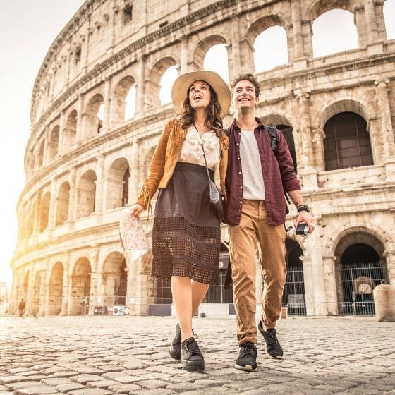 A cute couple stands next to the Colosseum in Italy. 