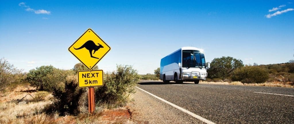 A bus on its way to Sydney on a two lane asphalt road in rural Australia with kangaroo crossing sign.